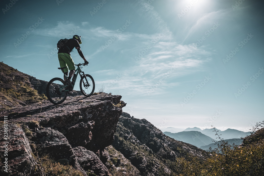 mountain biker riding up a large rock deep in the alps with sun and ...