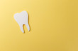 White tooth on yellow background with copy space. Oral dental hygiene. Teeth whitening. Dental health concept. Oral care, teeth restoration. Dentist day concept. Flat lay. Top view