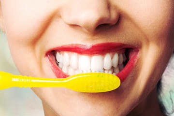 Wall Mural - Female brushing teeth with yellow brush, close up