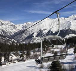 Chair-lift at ski resort and snowy winter mountains in nice sun day