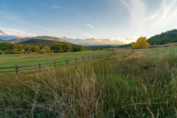 The sun is about to set over a ranch in the colorado mountains filled with cows and surrounded by fences