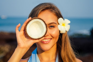 Portrait of beautiful girl close-up snow-white smile,blue eyes and perfectly clean skin holding an open dry coconut near face.female model on the beach happy tropical paradise coco nut oil face care