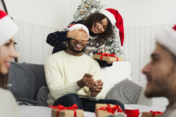 Wall Mural - Christmas holiday couple happy young woman surprise boyfriend,covering mans eyes, isolated over white background wear red new year hats and shirts