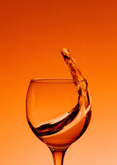 Splash of wine in a glass. Drink in glass on a orange backgroun