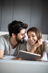 Canvas Print - Happy young couple looking a tablet together and laughing while lying on the bed