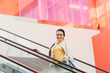 attractive girl with shopping bags smiling and looking at camera on escalator