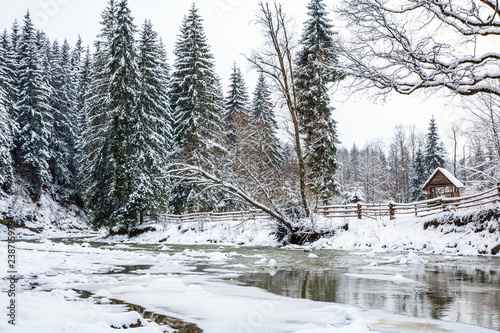 Zdjęcie XXL zamarznięta rzeka górska w świerkowym lesie śnieżnym, ogrodzenie i altanka na brzegu