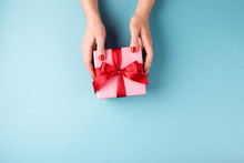 Overhead View On Female Hands With Red Manicure Holding Pink Gift Box  With Red Bow On Blue Background. Minimal Styled Composition.