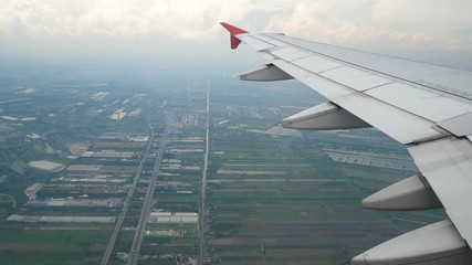 Wall Mural - 4K footage. traveling by air. aerial view through an airplane window at landing time. wing airplane moving for change to lower level direction and rustic view with rice field.