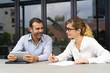© Mangostar - Portrait of male and female colleagues communicating in office. Young Caucasian businesswoman talking to mid adult bearded man with digital tablet. Corporate concept