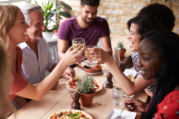 Friends laughing at a dining table in a cafe making a toast