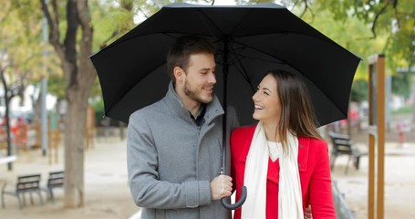 Wall Mural - Front view of a happy couple walking and talking under the rain in winter