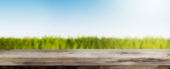 rustic wooden table against lush green field under blue sky wide background banner