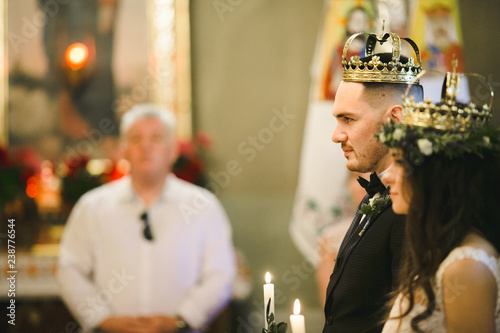 Fotografie, Obraz Happy bride and groom stand with crowns during ceremony in church