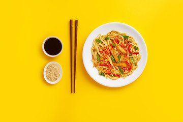 Noodles with fried chicken and vegetables on a yellow background. Flat lay with top view and copy space