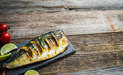 Wall Mural - Fried mackerel fillets with lime on black slate board, wooden background