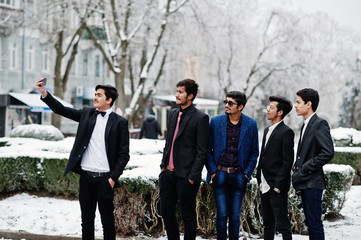 Group of 5 indian students in suits posed outdoor in winter day and making selfie on phone.