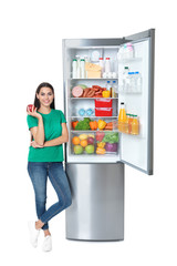 Wall Mural - Young woman with apple near open refrigerator on white background