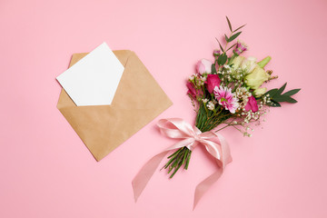 Valentines day composition: bouquet of flowers, kraft envelope with greeting card lay at pink background. Woman's day card template, flat layout, top view, overhead.