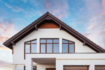 Photo of beautiful comfort and new house with brown roof large windows and white wall against calm blue sky