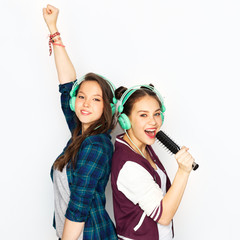 people, leisure and technology concept - smiling teenage girls in earphones listening to music and singing to hairbrush and having fun over white background