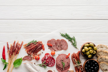 Wall Mural - top view of arrangement of various meat snacks and olives on white wooden backdrop