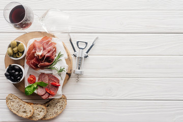 Wall Mural - flat lay with glass of red wine, pieces of bread and assorted meat snacks on white wooden tabletop