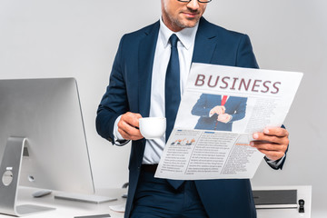 Wall Mural - cropped image of businessman holding cup of coffee and reading business newspaper isolated on white