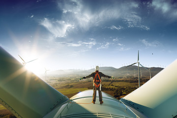 Happy engineer feel success after good work. He standing a top of windmill and looking beautiful sunset