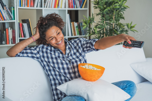 Fotografie, Tablou Black woman watching tv at home and holding a remote control