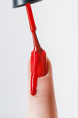 Wall Mural - partial view of woman applying dripping red nail polish on fingernail isolated on grey