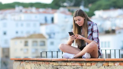 Sticker - Excited teen finding online content on a smart phone sitting on a ledge on vacation