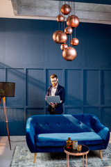 Portrait of an elegant businessman sitting with laptop on the couch at the luxury blue office interior