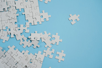 Fragment of a folded white jigsaw puzzle and a pile of uncombed puzzle elements against the background of a blue surface.