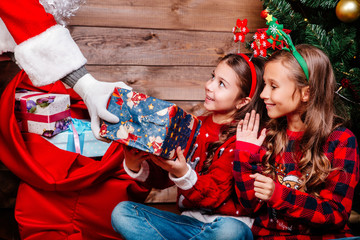 Santa Claus giving a present to two little cute sisters near Christmas tree at home