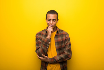 young african american man on vibrant yellow background looking down with the hand on the chin