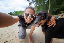 Young Beautiful Happy Joyful Girl Woman Having Fun Taking A Selfie On A Mobile Phone With Her Dog On The Beach Along The Sand