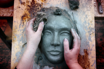 The hands of the sculptor mold the clay mask