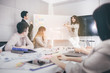 © Yingyaipumi - Businesswoman presenting to colleagues at a meeting.Successful team leader and business owner leading informal in-house business meeting. Businessman working on laptop in foreground.
