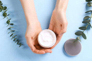 Wall Mural - Moisturizing care skincare face cream for healing complicated troubled skin type in an open jar with visible texture. Copy space, close up, background, flat lay, top view. Eucalyptus leaf decoration.