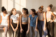 Six attractive different slim girls standing together in a row talking enjoy pleasant conversation. Multiracial women in activewear with yoga mats waiting workout at sports studio in the sunny morning