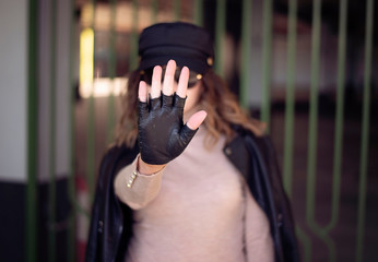 Street fashion outdoor photo of woman with dark hair in black leather jacket and sunglasses in defocus. Woman gesturing STOP with her hand image