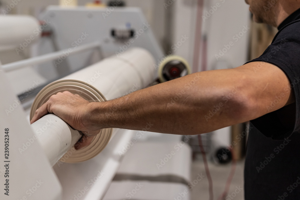 Operating a big printing machine and laminator, armed with red rolls and vinyl transparent film. Industrial worker, technical staff.