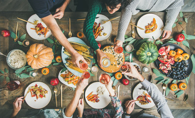 Wall Mural - Vegan or vegetarian Thanksgiving, Friendsgiving holiday celebration. Flat-lay of friends eating and clinking glasses at Thanksgiving Day table with pumpkin pie, vegetables, fruit and wine, top view
