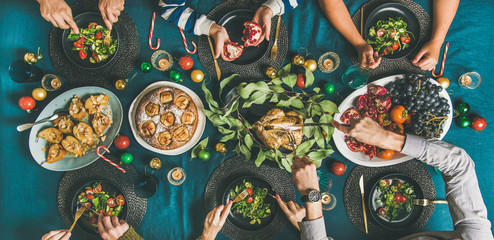 Wall Mural - Company of friends of different ages gathering for Christmas or New Year party dinner at festive table. Flat-lay of human hands eating meals and celebrating holiday, top view