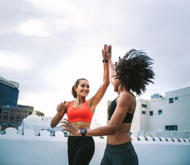 Wall Mural - Cheerful fitness women giving high five while jogging on rooftop