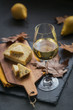 A glass of white wine served with cheese in a cutting board on dark background
