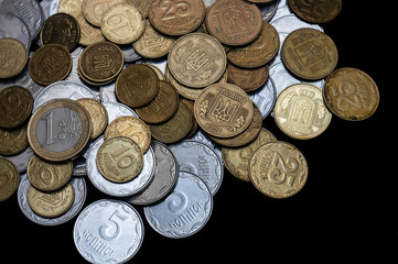 Ukrainian coins with one euro coin isolated on black background. Close-up view. Coins are located at the left side of frame. A conceptual image.