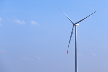 One single windmill turbine with blue sky in background. Renewable energy wind turbine