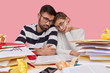 © WHstudio Leushin N - People, collaboration and tiredness concept. Unhappy woman and man sit closely, have dejected facial expressions, fatigue of preparing diploma paper, have much paper work, isolated over pink wall